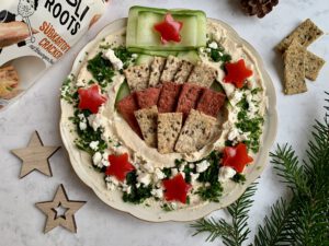Hummus-Kranz mit Holiroots Crackern in den Sorten Rote Bete und Pastinake als herzhafter Weihnachtssnack für Gäste.