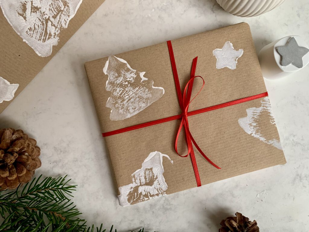 Fertig eingepacktes Geschenk mit Geschenkpapierrolle im Hintergrund – DIY-Geschenkverpackung mit Kindern