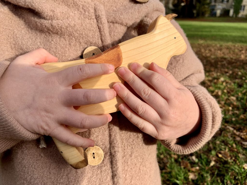 Kleinkind drückt eine Sägefisch-Holzkuh an sich – robustes, nachhaltiges Holzspielzeug.