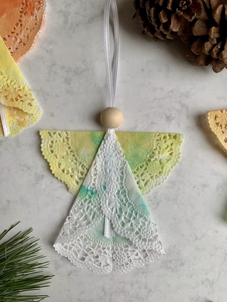 fertiger-tortenspitzen-engel-diy-weihnachtsbasteln-kleinkinder.jpg Fertig gebastelter Weihnachtsengel aus bemalter Tortenspitze, Holzperle und Band. Einfache Weihnachtsbasteln mit Kleinkindern.