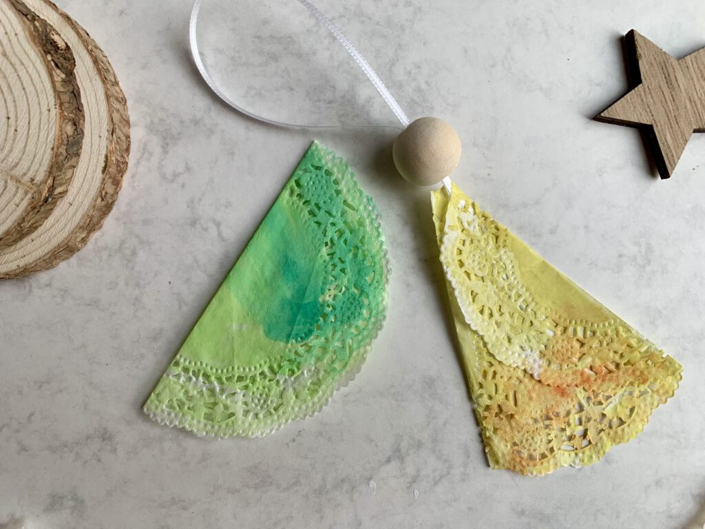 engel-basteln-nahaufnahme-tortenspitze-band-holzperle.jpg Nahaufnahme eines Bastelschritts: Tortenspitze, Band und Holzperle für einen Weihnachtsengel. Schnelle Weihnachtsengel basteln mit Kindern.