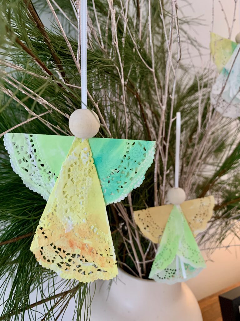 weihnachtsengel-aus-tortenspitze-falten.jpg Zwei selbst gebastelte Tortenspitzen-Engel hängen an einem weihnachtlichen Adventsgesteck. Einfach Geschenke basteln mit Kleinkindern.