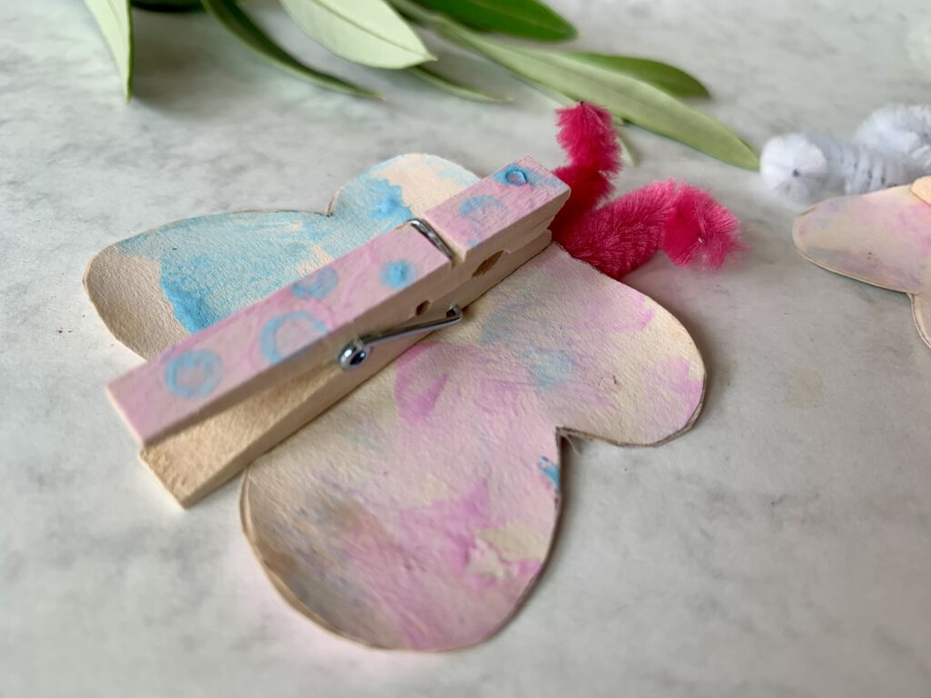 Detailaufnahme eines Schmetterlings, der aus einer Wäscheklammer und Tonpapier gebastelt wurde. Gestaltet von einem Kleinkind mit Fingerfarben fürs Basteln im Frühling