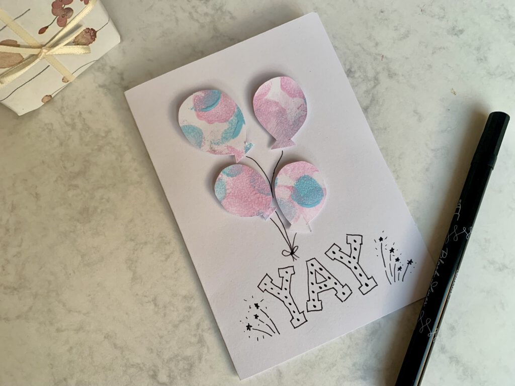 geburtstagskarte-basteln-aus-kinderzeichnungen Aus Kinderzeichnungen in Pastellfarben wurden kleine Luftballons ausgeschnitten und auf eine Klappkarte geklebt. Zusammen mit dem Schriftzug "Yay" entsteht eine hübsche Grußkarte. Ideal als einfache Bastelidee für Kleinkinder.