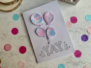 Basteln mit Kleinkindern: Eine einfache Geburtstagskarte, beklebt mit bunten Luftballons, die aus einer Kinderzeichnung ausgeschnitten wurden.