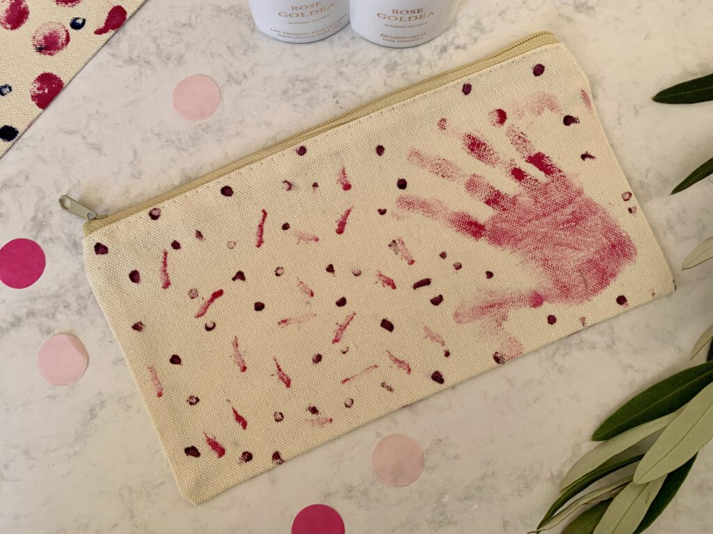 Selbst gestaltetes Kosmetiktäschchen aus Canvas mit buntem Handabdruck eines Kleinkinds und Konfetti-Muster