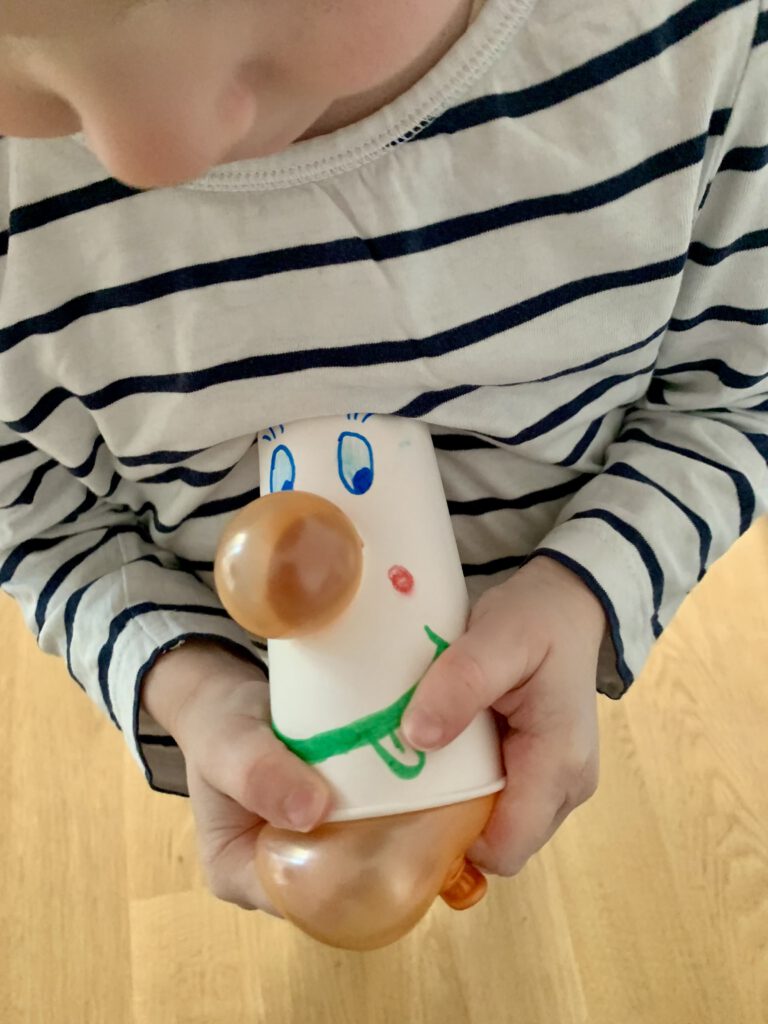 Kleinkind hält einen selbst gebastelten Clown mit Zaubernase und drückt den Luftballon