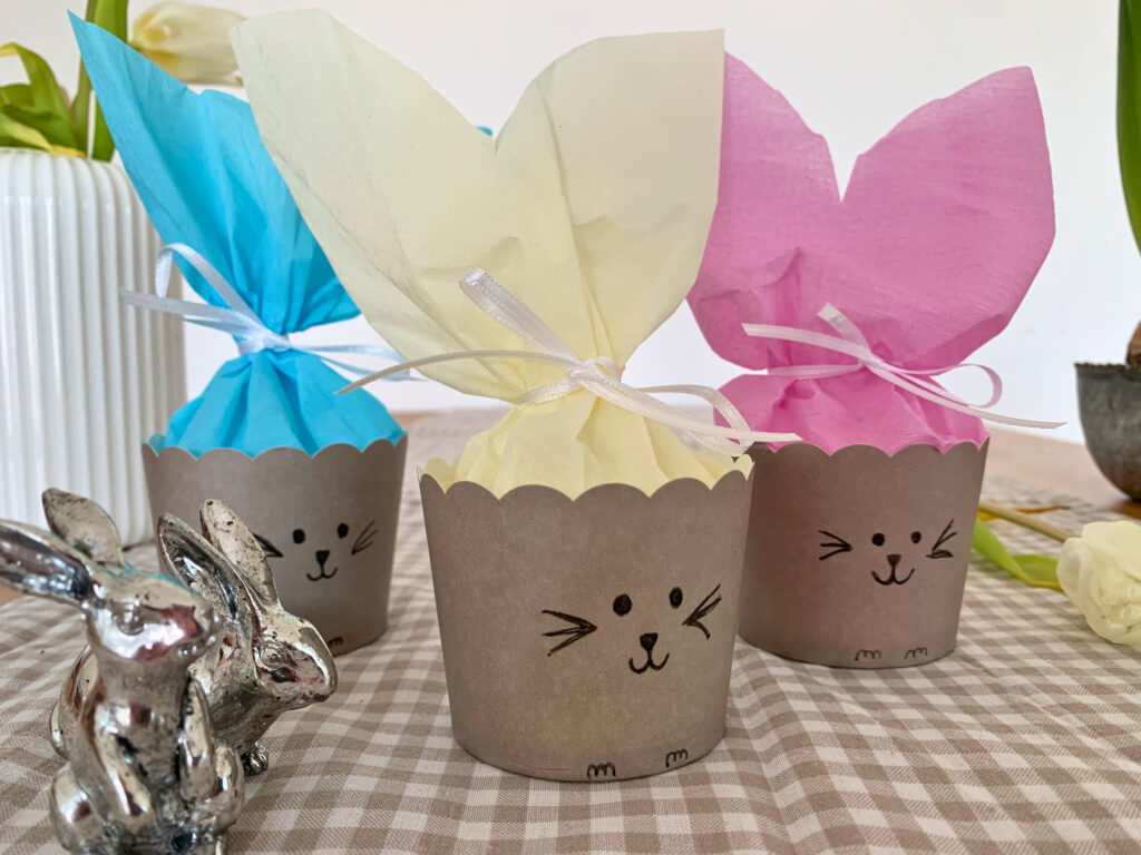Idee für ein kleines Ostergeschenk: Drei selbstgebastelte Osterkörbchen in Hasenform mit beigem, blauem und rosafarbenem Krepppapier