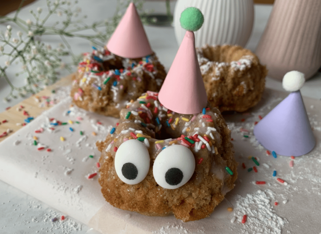 Mini-Gugelhupf bzw Muffin mit rosa und lila Partyhut sowie bunten Zuckerstreuseln für den Kindergeburtstag dekoriert