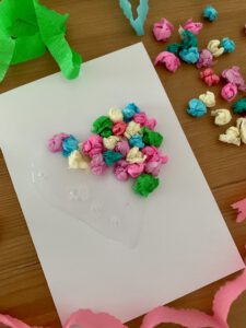 Blankokarte mit Kleber und teilweise aufgeklebten Krepppapierkügelchen. Schritt für Schritt Anleitung für eine selbst gebastelte Herzkarte – einfache Kartenidee zum Basteln mit Kleinkindern ab 2 Jahren