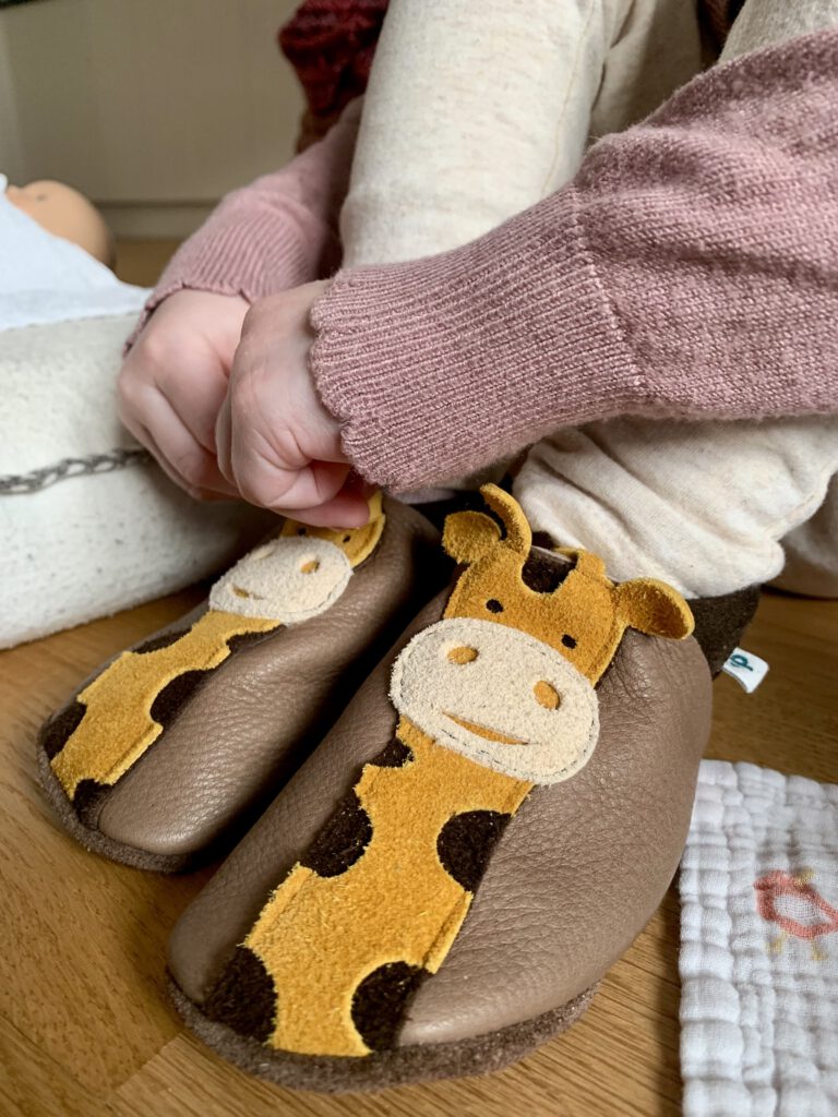 Kleinkind zieht selbstständig Pantolinos Hausschuhe aus weichem Naturleder an