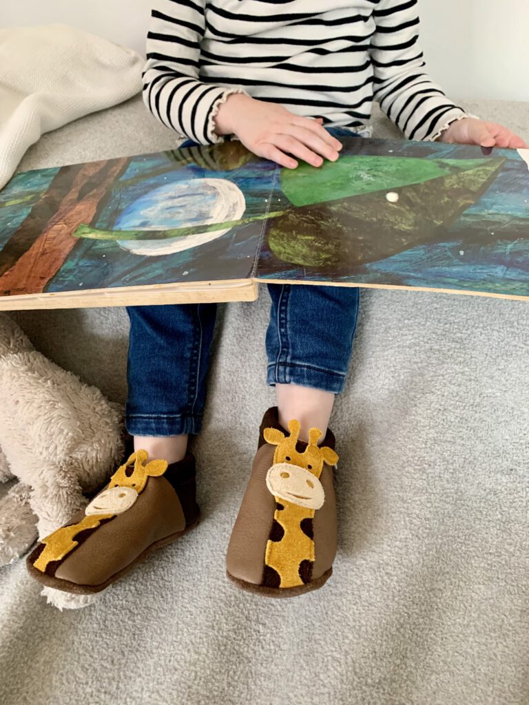 Kleinkind liest ein Buch und trägt Pantolinos Hausschuhe aus nachhaltigem Naturleder