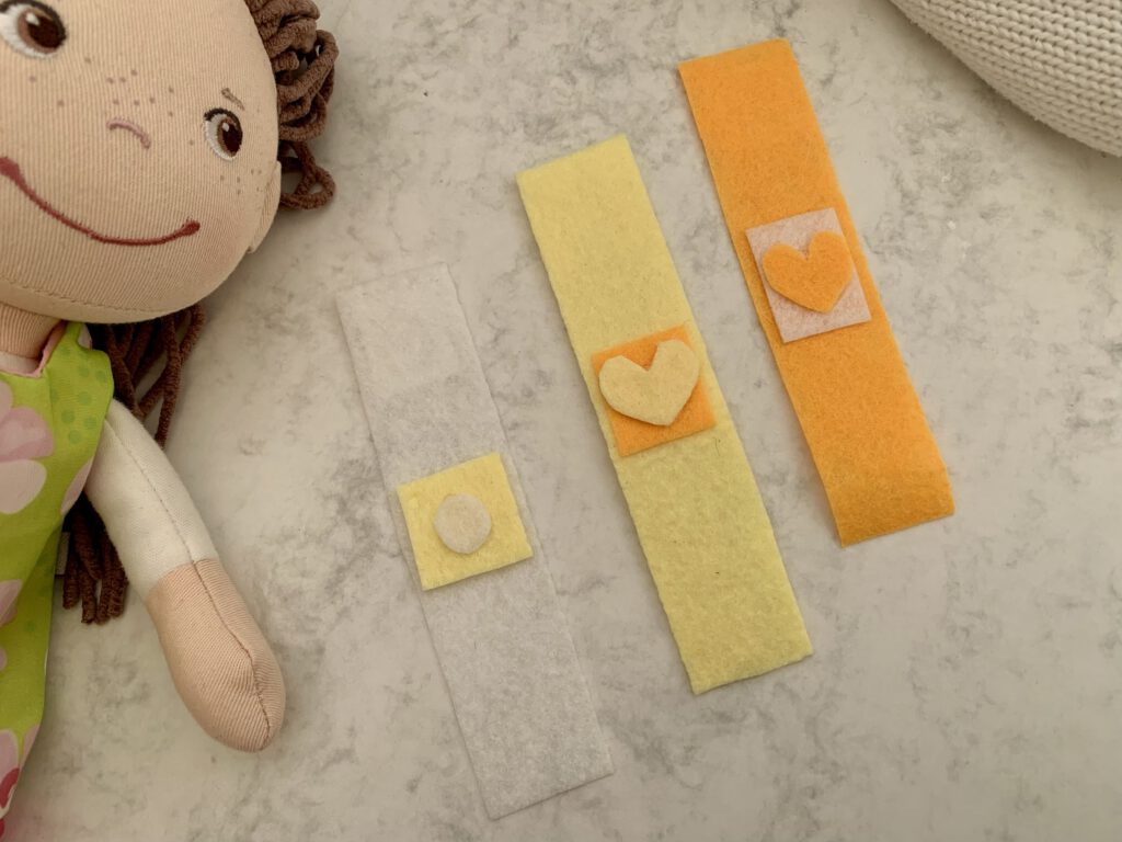 Drei selbstgemachte Spielpflaster mit unterschiedlicher Deko aus Filz, im Hintergrund eine Puppe