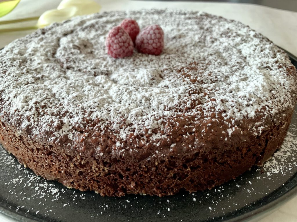 Saftiger Schokokuchen ohne Industriezucker und ohne Mehl mit Puderzucker und frischen Himbeeren, schräg von oben fotografiert.