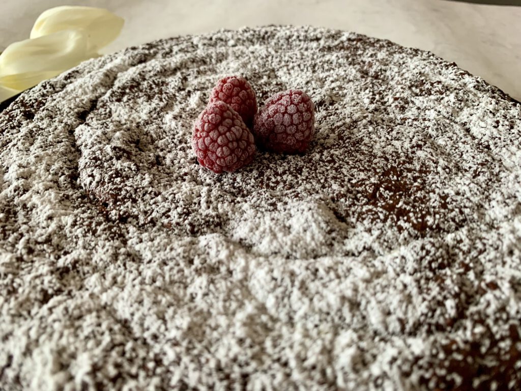 Schokoladiger Kuchen ohne Mehl, mit Puderzucker bestäubt und mit Himbeeren dekoriert, Aufnahme schräg von oben.