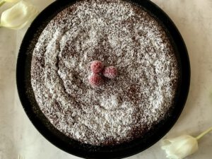 Saftiger Schokokuchen ohne Industriezucker mit Puderzucker und Himbeeren, Draufsicht auf den ganzen Kuchen.