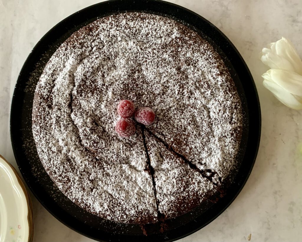 Glutenfreier Schokokuchen ohne Industriezucker, mit Puderzucker bestäubt und Himbeeren dekoriert, von oben fotografiert.