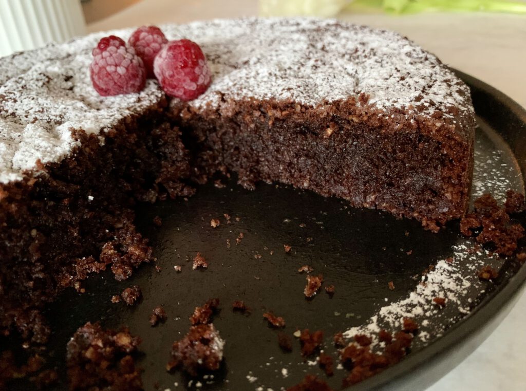 Angeschnittener saftiger Schokokuchen ohne Industriezucker und ohne Mehl mit Puderzucker und Himbeeren.