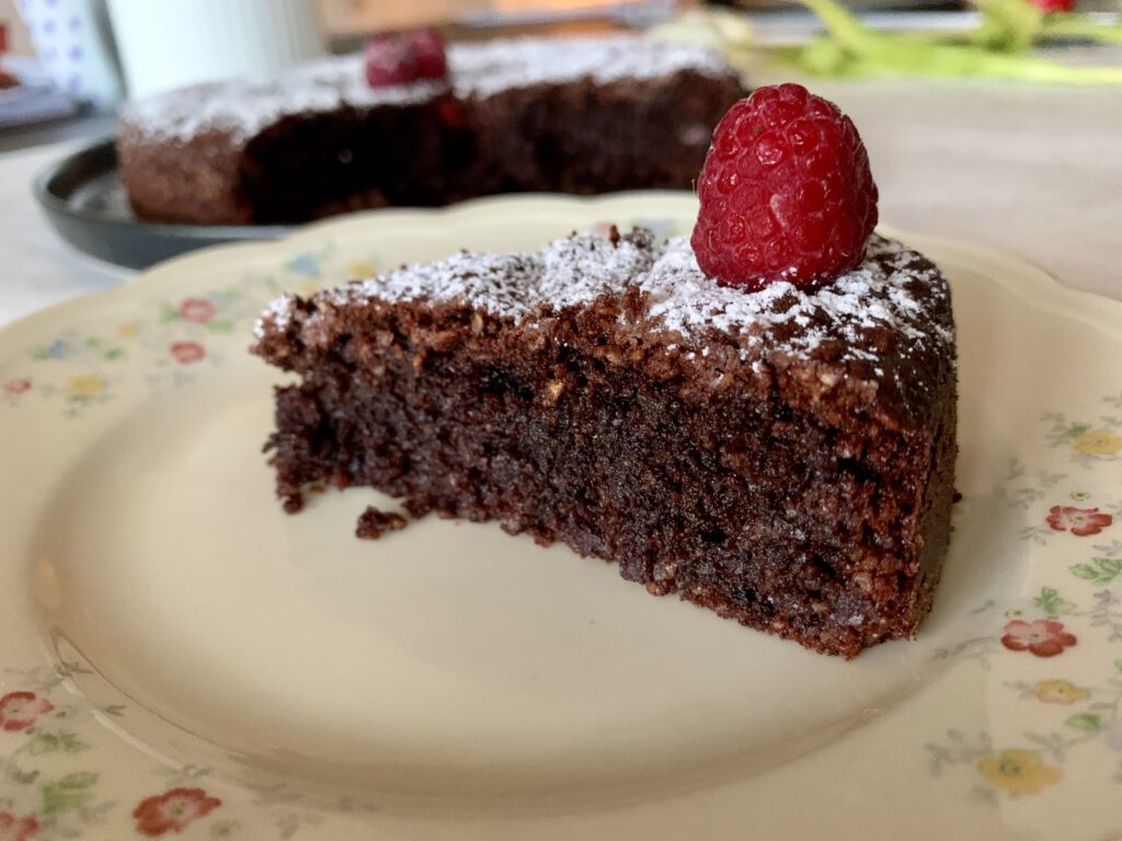 Ein Stück saftiger Schokokuchen ohne Industriezucker auf einem Teller, mit Puderzucker und Himbeeren serviert.
