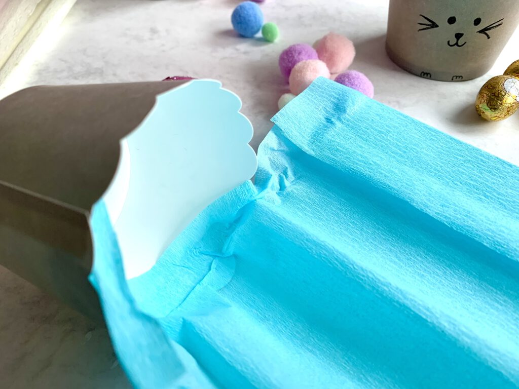 Krepppapier wird am Rand eines Muffinförmchens befestigt für das Osterkörbchen