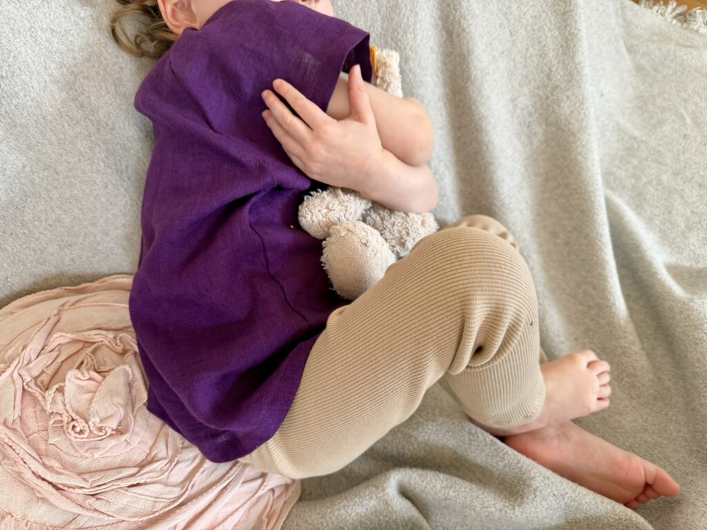 Kleinkind kuschelt mit Teddy und trägt Kurzarmbluse und Ripp Leggings aus Bio-Baumwolle