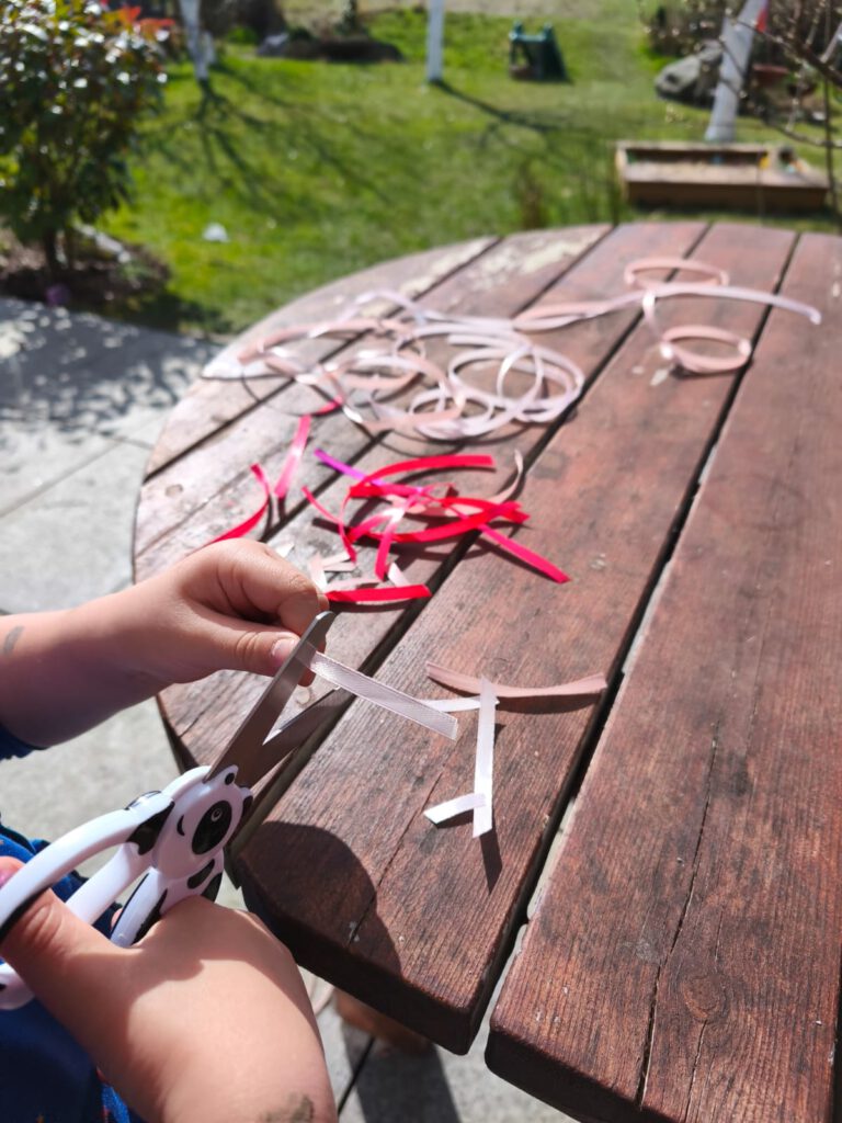 kleinkind-schneidet-bunte-baender-osterbasteln Kleinkind schneidet bunte Bänder für Osterdeko im Garten
