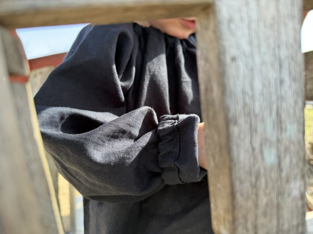 Detail der Leinenbluse für Kinder mit elastischem Halsausschnitt und gerafften Ärmeln, ideal als Outfit für den Frühling