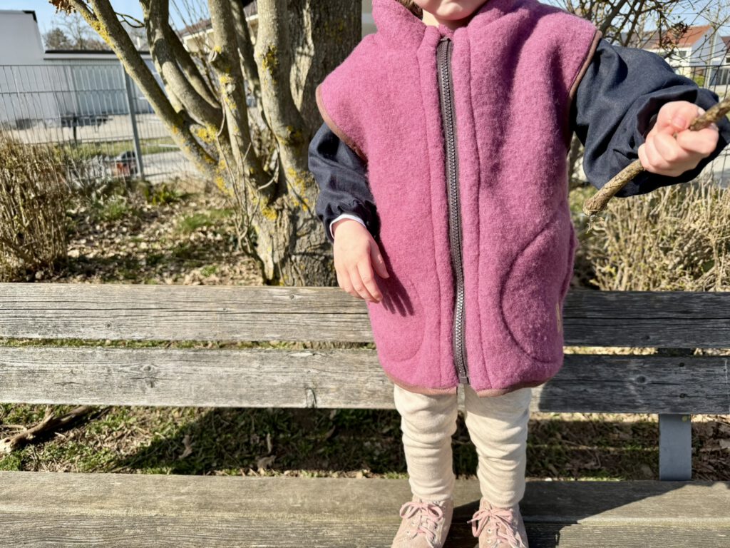 Kind steht auf einer Bank auf dem Spielplatz mit nachhaltigem Frühlingsoutfit aus Wolle und Leinen