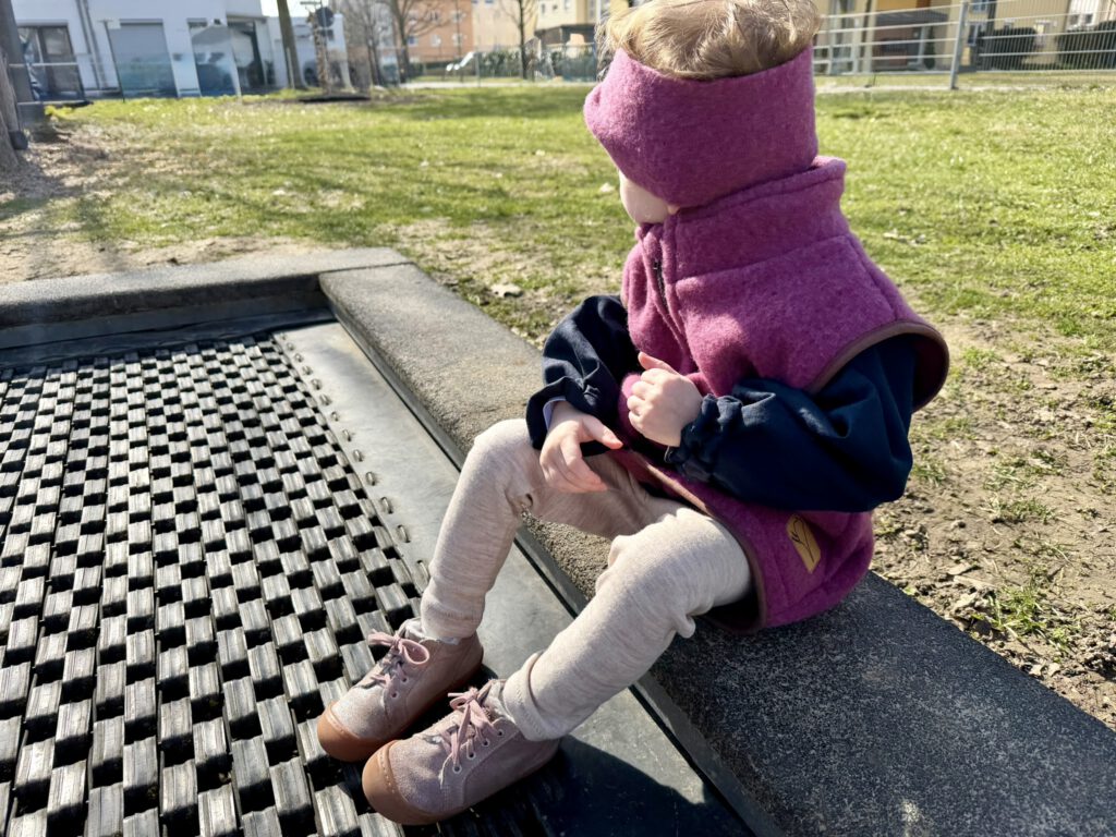 Kleinkind im Frühling auf dem Trampolin mit nachhaltigem Frühlingsoutfit aus Wollfleeceweste, Stirnband und Leggings von Buchfinkkleidung
