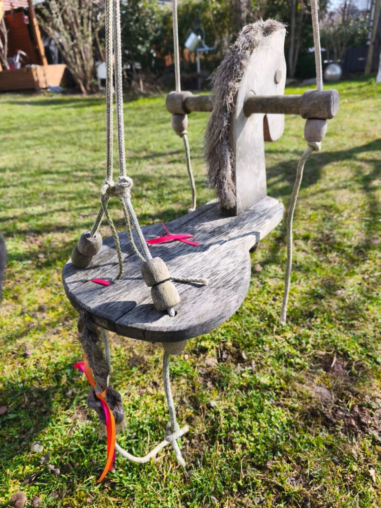 osterdeko-garten-schaukeltier-mit-bunten-baendern Frühlingsdeko im Garten mit bunten Bändern an einer Kinderschaukel